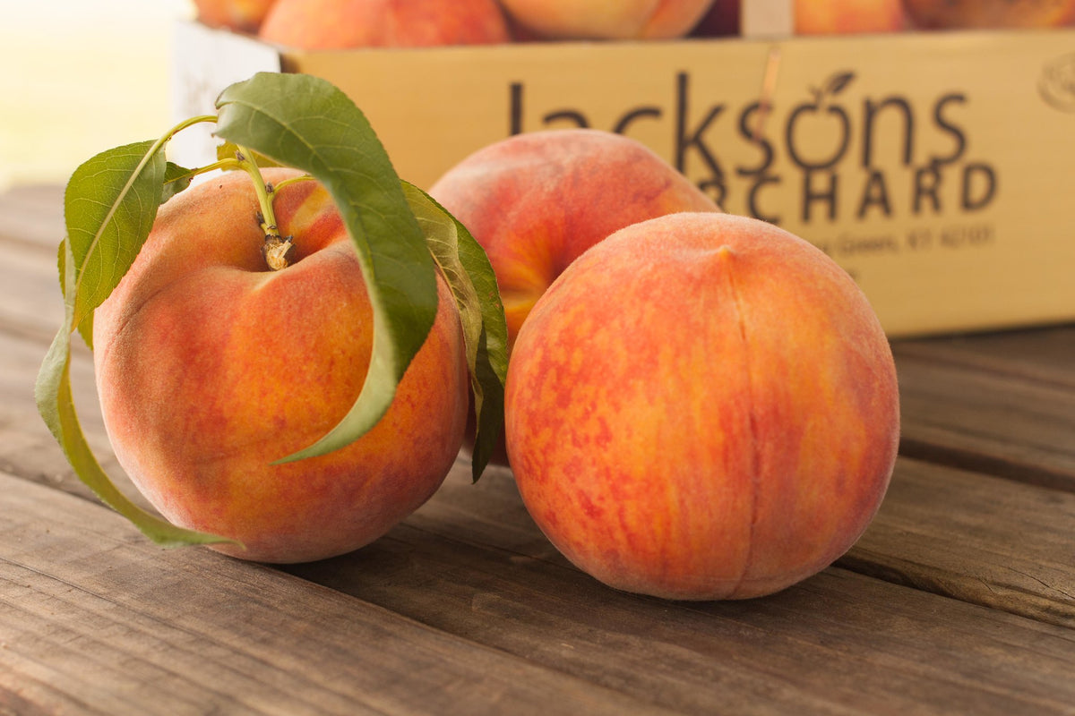 Ripe Glowingstar peaches on a table in front of a Jackson's Orchard box